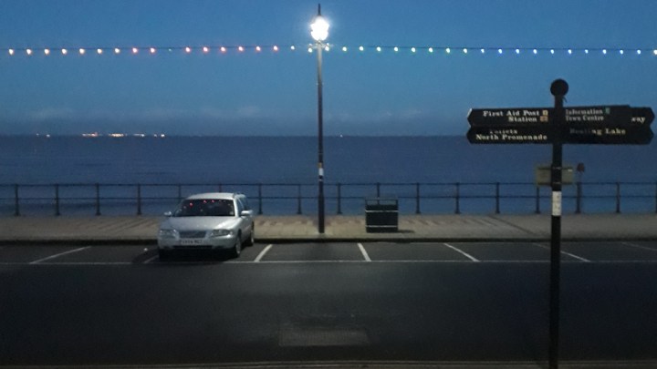 View from Cleethorpes central promenade, looking across the sea road out into the estuary at dusk with the tide in. Christmas lights border the top of the shot.